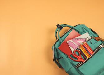 Back to school concept.Top view of backpack with school supplies on orange  background