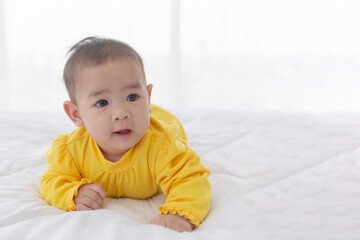 An Asian infant lying prone on a clean white bed.