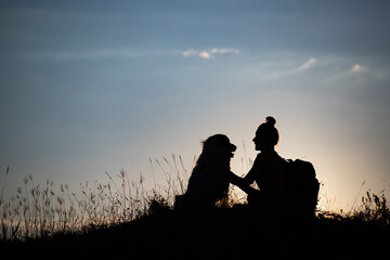 Woman with her dog sitting on the hill in the sunset.