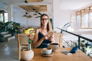 Cheerful woman with book in hands sitting in cafe