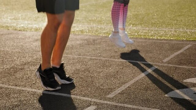A man and a girl jump rope at the stadium in the summer. Close-up of feet in athletic shoes.