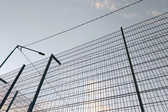 High wire mesh fence in restricted area on blue sky background.