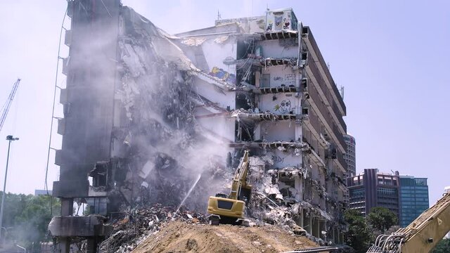 Demolition of an abandoned office building covered with graffiti, heavy machinery at work, urban background - old vs new.