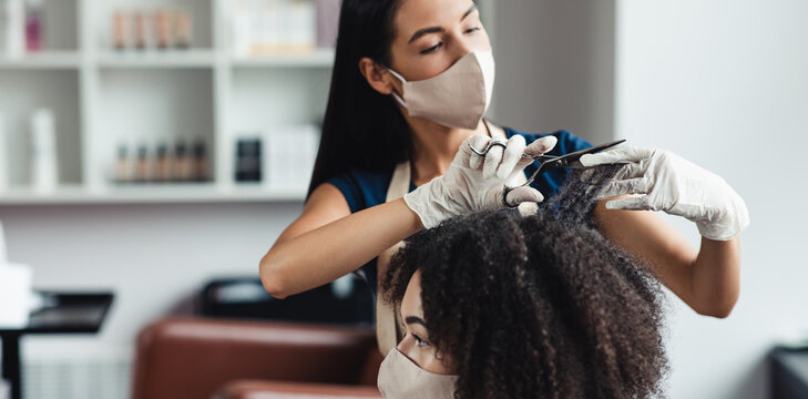 African american woman getting haircut from master, wearing protective masks, panorama