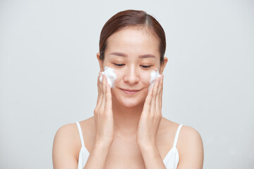 Portrait of young Asian woman applying foaming cleanser against white background.