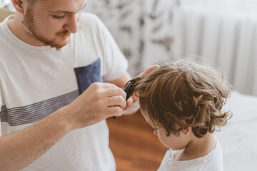 Father cuts her son hair in the room. Family during quarantine, Scissors and a comb in male hands
