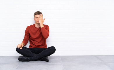 Young handsome man sitting on the floor covering a eye by hand