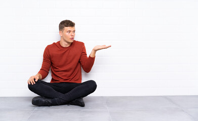 Young handsome man sitting on the floor holding copyspace imaginary on the palm