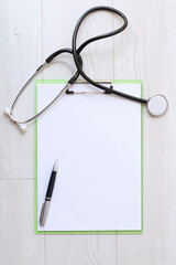 Blank medical clipboard with stethoscope on wood background. 