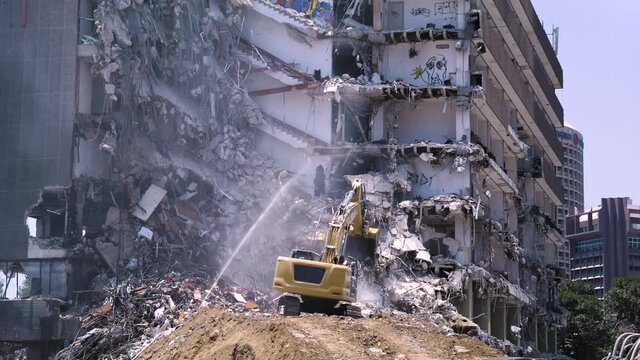 Demolition of an abandoned office building covered with graffiti, heavy machinery at work, urban background - old vs new.