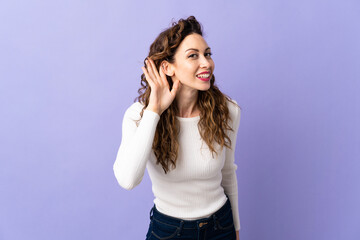 Young caucasian woman isolated on purple background listening to something by putting hand on the ear