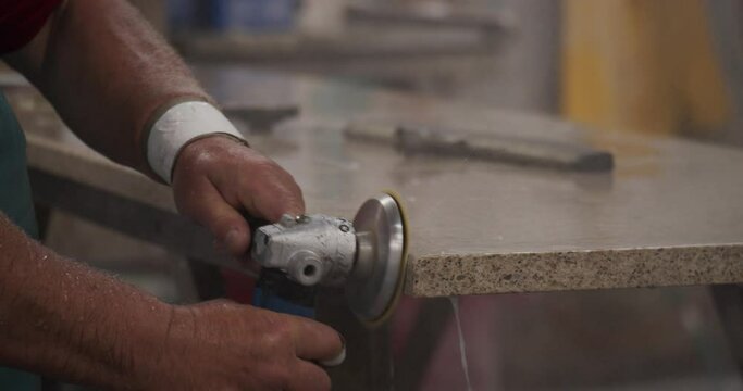 Skilled stone cutter bevelling granite countertop with liquid cooled orbital sander. Kitchen cabinetry. 