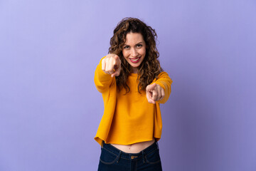 Young caucasian woman isolated on purple background pointing front with happy expression