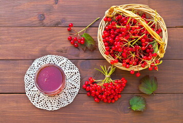 Beautiful rustic still life with red berries of viburnum in wicker basket and viburnum jam in a jar on a lace crocheted napkin on wooden background. Healthy food. Copy space, flat lay, close-up