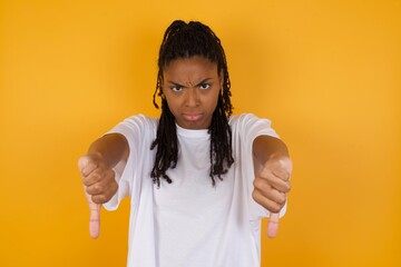 Young dark skinned woman with braids hair wearing white t-shirt over yellow background being upset...