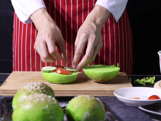 Hands of chef preparing hamburger made for green veggie bread on wooden cutting board, healthy  fast food concept