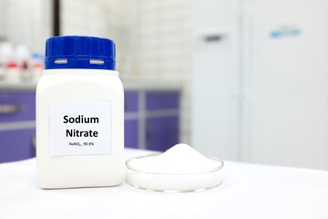 Selective focus of a bottle of sodium nitrate preservative compound beside a petri dish with white...