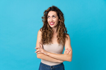 Fototapeta premium Young caucasian woman isolated on blue background looking up while smiling