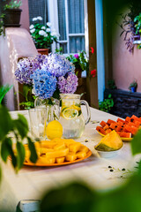 Watermelon triangle slices, yellow orange Mellon slices and lemonade on a table. A vase with flowers in the background