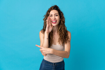 Fototapeta na wymiar Young caucasian woman isolated on blue background pointing to the side to present a product and whispering something