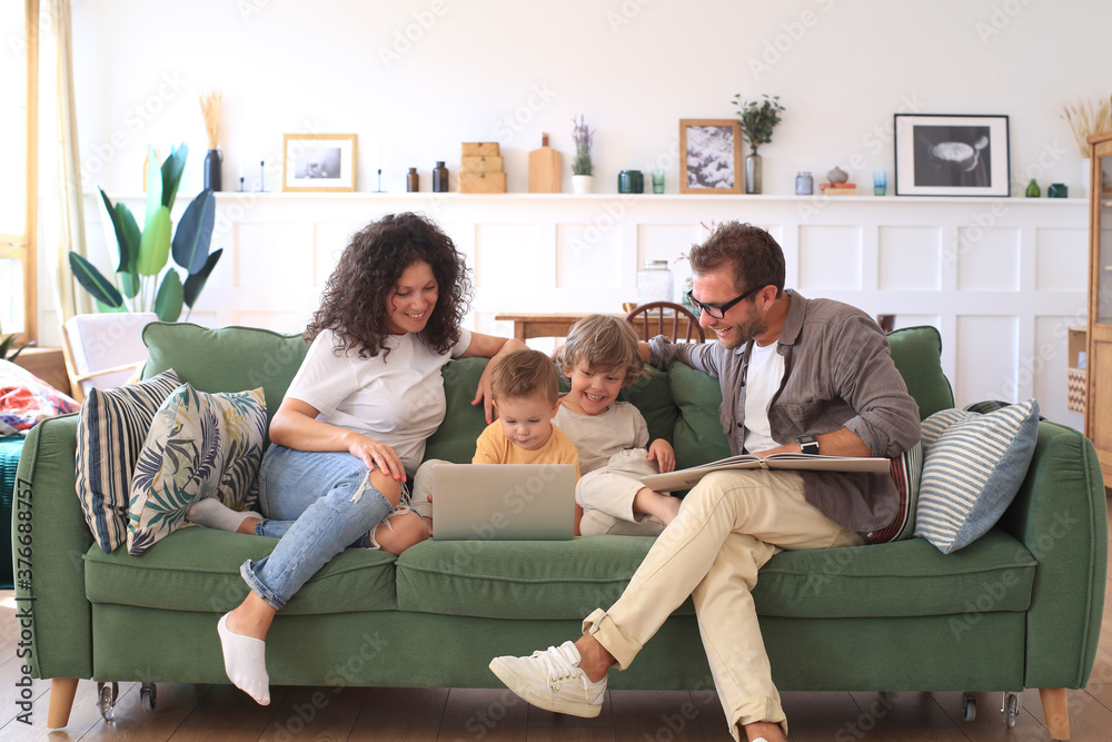 Wall mural Young beautiful happy family relaxing on the sofa and look at the laptop at home.