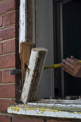 Crowbar being used to remove an old wooden window frame in brick wall during house renovations