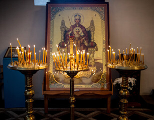 A large icon of the Virgin Mary is illuminated by many yellow candles
