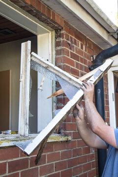 Workman Removing Old Wooden Window Frame From A Brick Wall During Home Renovation
