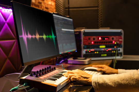 male music producer hands arranging a song on midi keyboard, computer and professional equipment in home recording studio