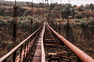 Obraz premium Old iron non-functioning suspension bridge over a dried river side view. Old pedestrian bridge in Moldova. 