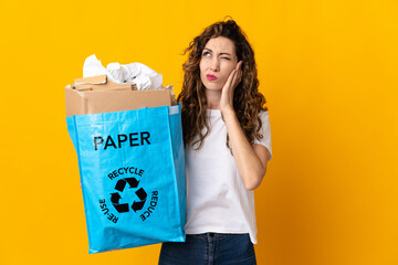 Young woman holding a recycling bag full of paper to recycle isolated on yellow background frustrated and covering ears