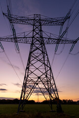 Silhouette of electricity tower construction and power lines against a colourful orange and magenta blue purple sunset sky