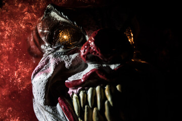 Spooky Clown head on wooden table. Evil clown head smiling on dark foggy background. Halloween...