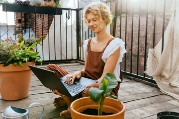 Charming woman housewife browsing internet with laptop, sitting on terrace outdoor. Blond haired female gardener watching gardening tutorials.