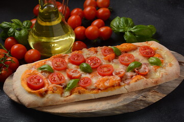Flatbread pizza garnished with fresh cherry tomatoes,basil,cheese and olive oil on wooden pizza board. Dark background