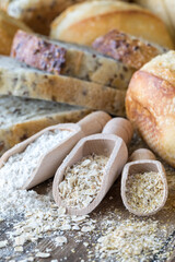 Close up of wooden scoops filled with flour, oats and oat bran and surrounded by bread.