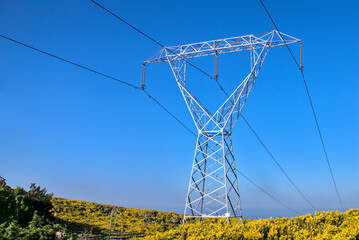 High voltage power lines. Power lines captured against the blue sky and May yellow flowering gorse in Ticknock, County Dublin, Ireland.