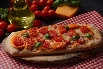 Flatbread pizza garnished with fresh cherry tomatoes,basil,cheese and olive oil on wooden pizza board. Dark background