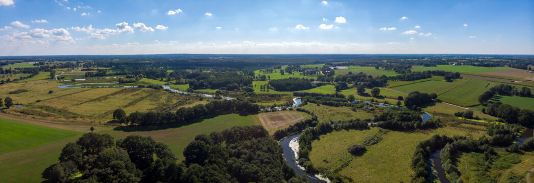 Wide aerial panorama of the river Regge meandering through the green Dutch Twente farmland landscape against a blue sky and clouds