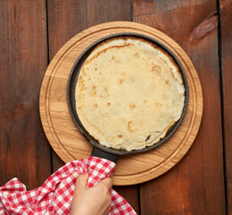 baked round big pancake in a black frying pan on a brown wooden table