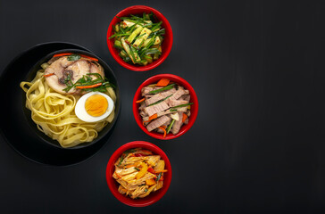 Noodles with pieces of meat and egg in a black plate and dim sum with different traditional snacks...