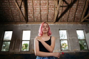 Fototapeta premium Young funky teenage girl with pink hair holding lollipop candy in abandoned building.