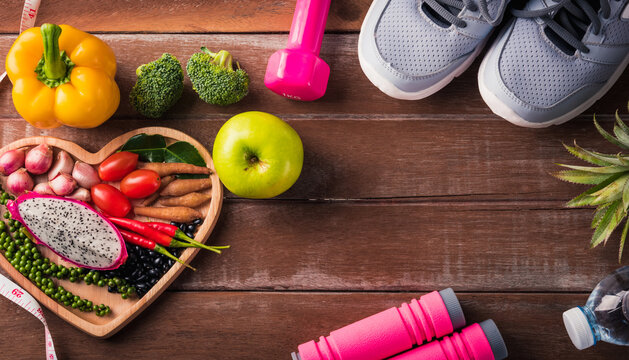 Top view of various fresh organic fruit and vegetable in heart plate and sports shoes, dumbbell and water, studio shot on wooden gym table, Healthy diet vegetarian food concept, World food day