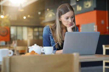 Young woman sitting at coffee shop and working on laptop