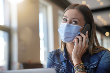 Young woman sitting at coffee shop and working on laptop with face mask