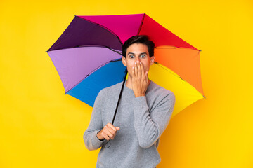 Man holding an umbrella over isolated yellow background with surprise facial expression