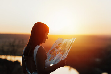 Traveler girl looking right direction on map, bright orange sunset light. Freedom and active...
