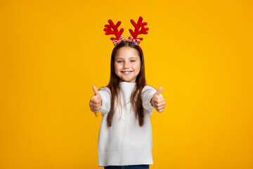 Children emotions. Smiling girl with horns and sweater showing thumbs up