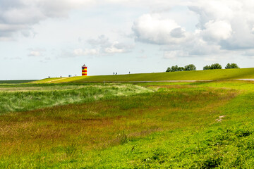 view on Pilsum lighthouse in the landscape of East Frisia with tourists walking around the dike and taking photographs
