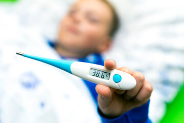 Close up ill young child or schoolboy, lying in bed shows a electronic thermometer, height of his fever